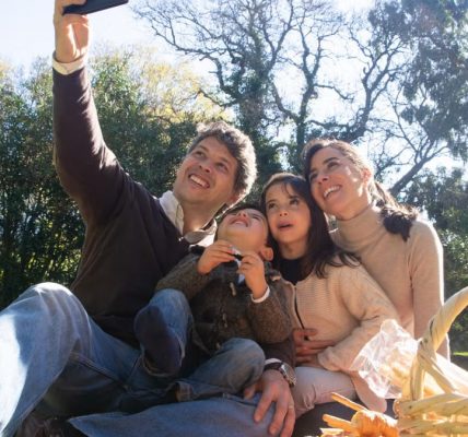 Happy family taking a selfie during a sunny picnic in a park.