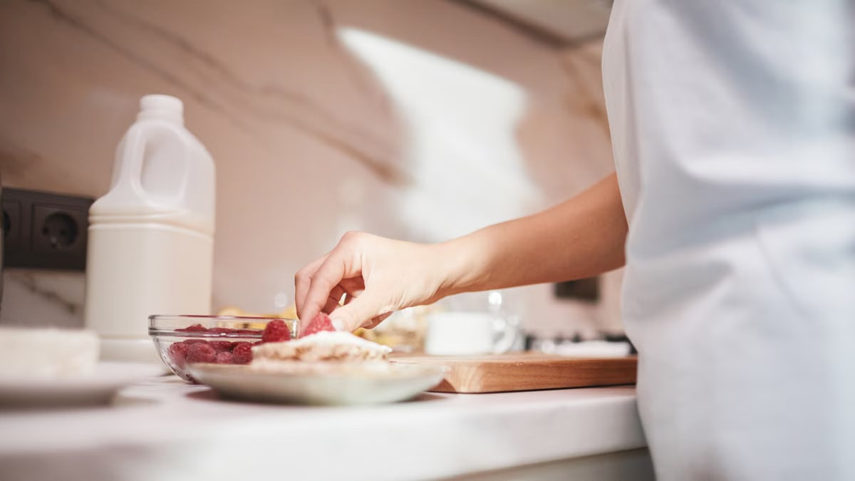 A close-up of a person preparing a raspberry dish on a kitchen counter.